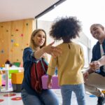 Une mère et un père accueillant chaleureusement leur enfant dans une salle colorée.