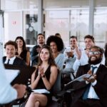 Un public souriant applaudit un orateur lors d’un colloque professionnel.