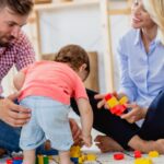 Un couple joue avec leur bébé en bas âge à l’aide de blocs de construction colorés.