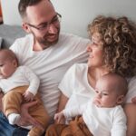Un père et une mère tiennent dans leurs bras leurs deux jumeaux, habillés de manière assortie.