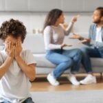 Un enfant cache son visage avec ses mains alors que ses parents se disputent en arrière-plan.