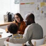 Un père et son fils en consultation avec une enseignante dans une salle de classe.