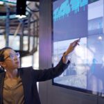 Femme en tenue professionnelle analysant des graphiques de données sur un écran numérique.