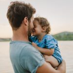 Un père et son enfant sourient tendrement en bord de lac au coucher du soleil