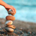Une main posant une pierre sur une pile de pierres équilibrées sur une plage