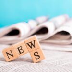 Des journaux empilés avec des blocs de bois formant le mot 'NEWS' en premier plan