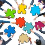 Des mains de plusieurs personnes tenant des pièces de puzzle colorées