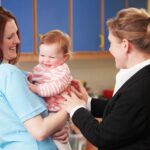 Une femme en tenue de travail sourit à une mère qui tient un bébé heureux dans ses bras, dans une crèche.