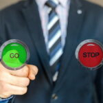 Une personne en costume 3 pièces pointe du doigt un bouteau vert avec inscription GO dessus, et de l'autre côté un bouton rouge indique STOP